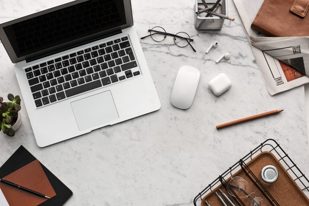 Overhead view of a laptop, glasses and office supplies on a desk